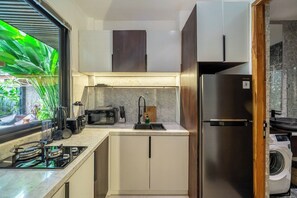 A compact kitchen with a built-in stove, a microwave, a sink, and a stainless steel refrigerator. - Modern 1BR Flat in Ubud w Pool, Patio & Kitchen (Kabupaten Gianyar)
