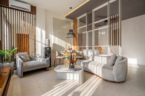 Ein modernes Wohnzimmer mit Sofa, Sessel, Couchtisch und einem Essbereich mit Stühlen und Tisch.