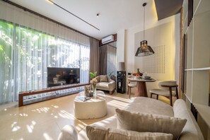 A modern living room with a sofa, a coffee table, and a TV. There is a dining area with a table and chairs. - Serene 1BR Stay in Ubud w Pool & Private Kitchen (Ubud)