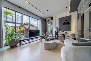 Ein modernes Wohnzimmer mit großem Fenster, einem Flachbildfernseher, einem runden Couchtisch und einer Couch.