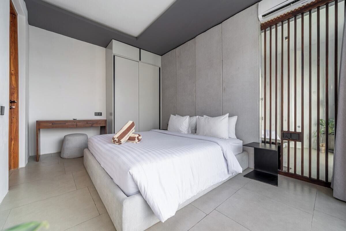 Ein modernes Schlafzimmer mit Bett, Nachttisch und Blick durch ein Fenster mit vertikalen Jalousien.