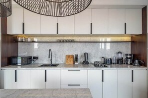Cozinha moderna com armários brancos, bancada de mármore e diversos eletrodomésticos, incluindo micro-ondas, torradeira e cafeteira.