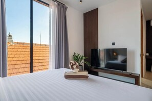 Quarto de hotel com uma cama grande, televisão de tela plana, planta em vaso e vista para a cidade pela janela.