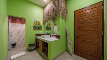 A bathroom with a green wall, a wooden door, a white sink, and a shower area.