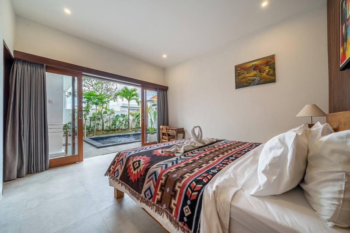 A bedroom with a bed, a desk, and a view of a garden through a sliding door.