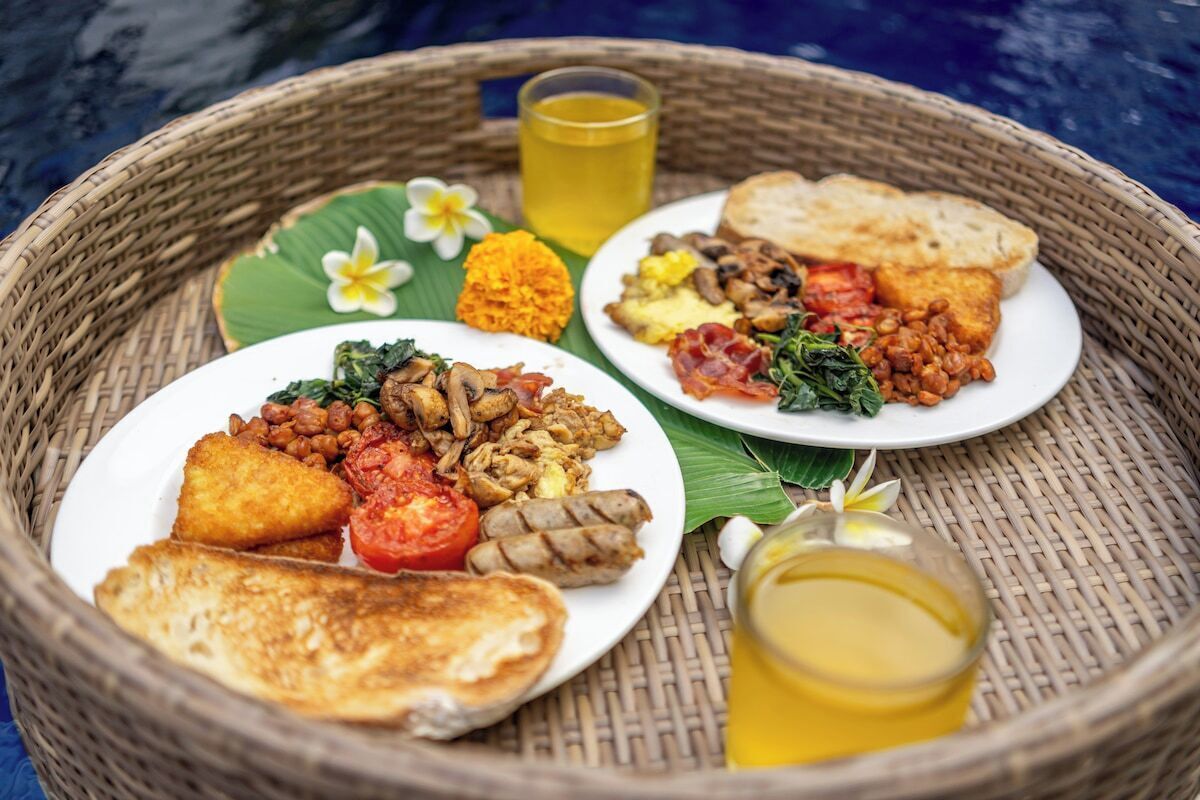 A wicker tray with two plates of food, a glass of yellow liquid, and a white flower.