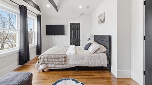 A bedroom with a bed, a flat-screen TV, a door, and a window.