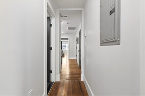 A hallway with white walls, wooden flooring, and a door leading to a room with a window.