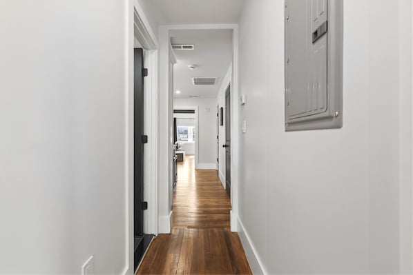 Un pasillo con paredes blancas, suelo de madera y una puerta que da a una habitación con ventana.