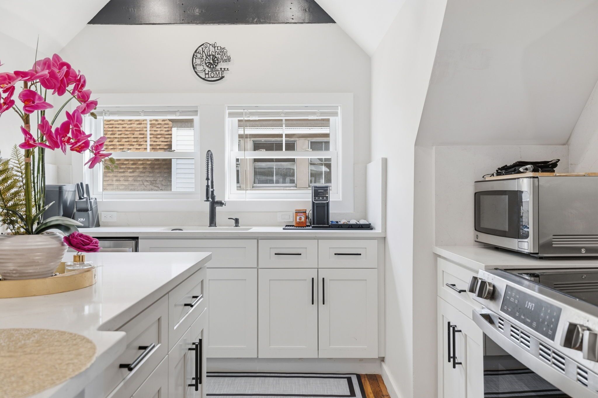 A modern kitchen with white cabinetry, a stainless steel microwave, and a coffee machine.