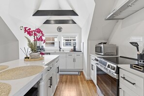 A modern kitchen with white cabinetry, a large island, and a built-in oven. - Bright and spacious 3BR Apt, gated 2 car parking, close to T station (Boston)