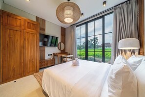 A bedroom with a large bed, a television, a wooden wardrobe, a desk, and a view of a green landscape through the window. - Serene 1BR Stay in Central Ubud w Pool & Kitchen (Gianyar Regency)