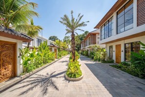 A pathway flanked by modern buildings with large windows, surrounded by lush tropical plants. - Serene 1BR Stay in Central Ubud w Pool & Kitchen (Gianyar Regency)