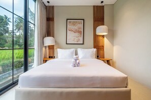 Quarto de hotel com uma cama grande, duas luminárias de cabeceira, uma obra de arte emoldurada na parede e vista para o verde pela janela.