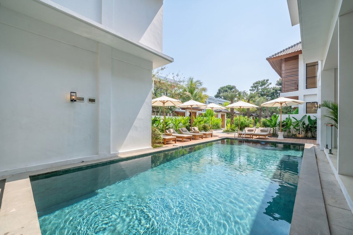 Une piscine entourée de verdure et d’un bâtiment blanc, avec des chaises longues et des parasols.