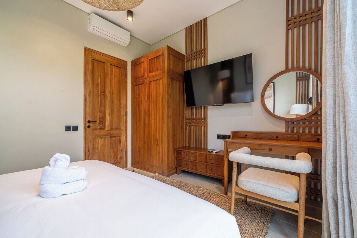 A hotel room with a bed, a wooden wardrobe, a television, a mirror, and a bathroom vanity.