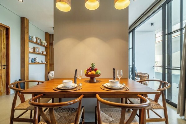 A dining area with a wooden table, chairs, and a fruit bowl centerpiece. - Cozy 1BR Apartment in Lush Ubud w Pool & Kitchen (Gianyar Regency)