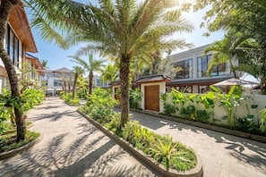 A pathway lined with palm trees and tropical plants, leading to a building with a traditional tiled roof. - Cozy 1BR • Ubud • Pool • Private Kitchen • Garden (Gianyar Regency)