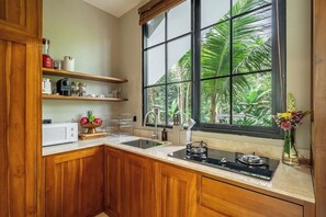 Una cocina con armarios de madera, un microondas blanco, un lavabo y una ventana con vistas a zonas verdes.