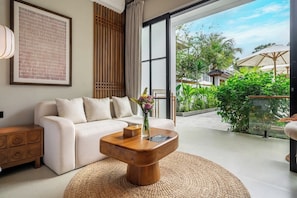 A modern living room with a sofa, a wooden coffee table, and a large window overlooking a garden. - Cozy 1BR • Ubud • Pool • Private Kitchen • Garden (Gianyar Regency)