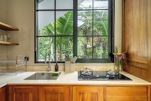 A kitchen with a large window, wooden cabinets, a stainless steel sink, and a built-in stove. - Cozy 1BR • Ubud • Pool • Private Kitchen • Garden (Gianyar Regency)