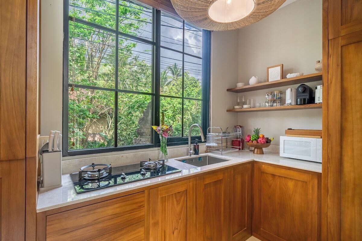 Cocina con armarios de madera, estufa a gas, lavabo y un amplio ventanal con vistas a zonas verdes.
