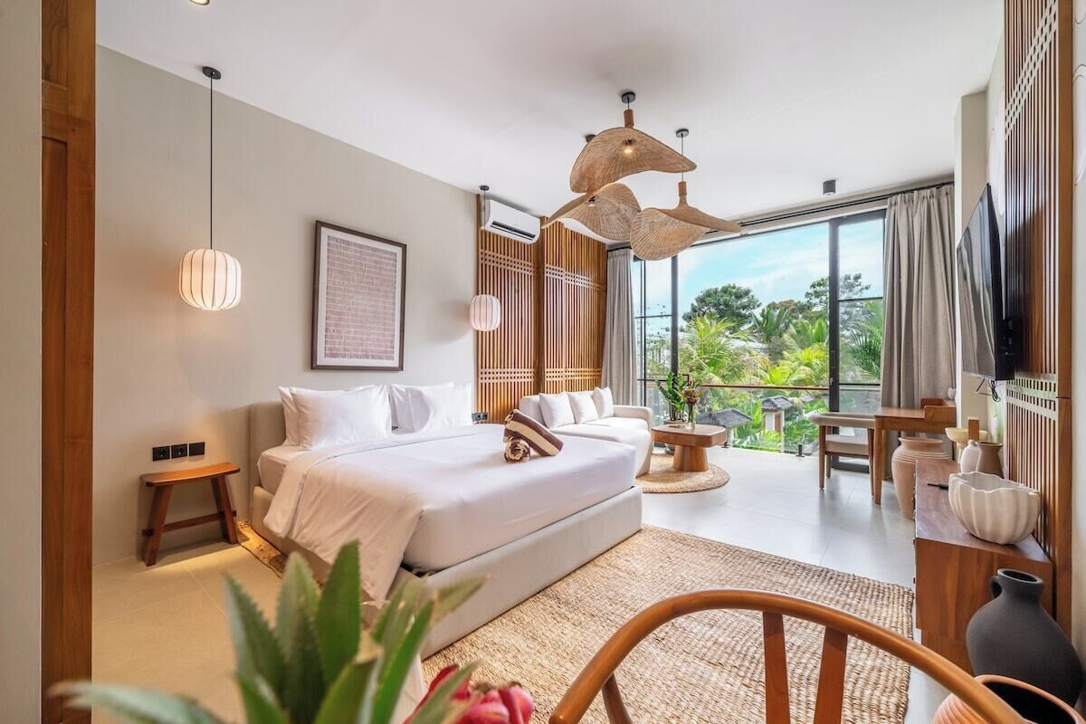 A modern bedroom with a large bed, a sitting area, and a view of greenery outside.