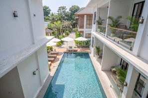 A swimming pool with a view of a residential area, surrounded by white buildings, and outdoor seating with umbrellas. - Luxe 1BR in Ubud w Pool, Private Kitchen & Balcony (Gianyar Regency)