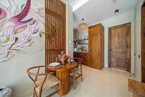 A dining area with a wooden table, chairs, and a decorative wall. - Luxe 1BR in Ubud w Pool, Private Kitchen & Balcony (Gianyar Regency)