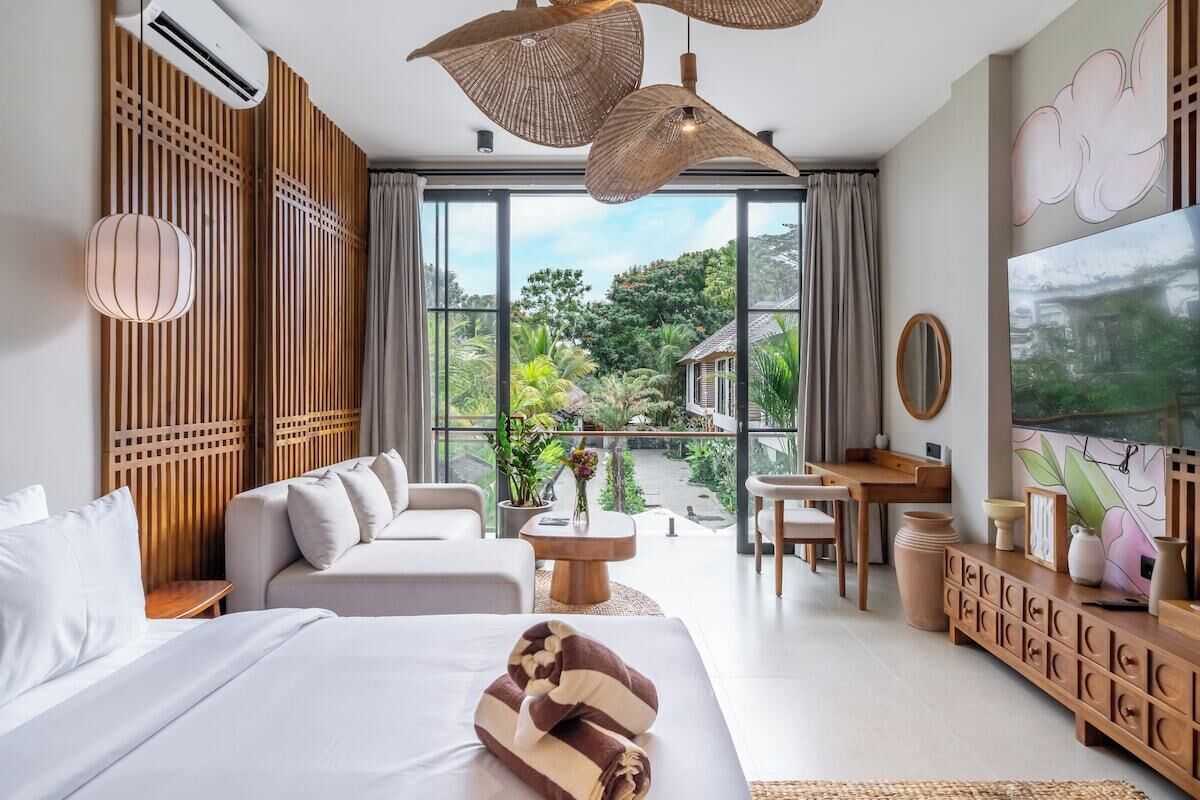 A modern hotel room with a large bed, a sofa, a dining area, and a view of the outdoors.