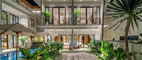 Un edificio de varios pisos con piscina, mobiliario exterior y abundante vegetación.