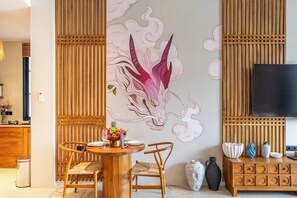 Een eetgedeelte met een houten tafel, stoelen, een wanddecoratie en een aan een houten paneel bevestigde televisie.