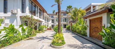 A hotel courtyard with a central palm tree, surrounded by lush greenery and modern buildings with large windows.