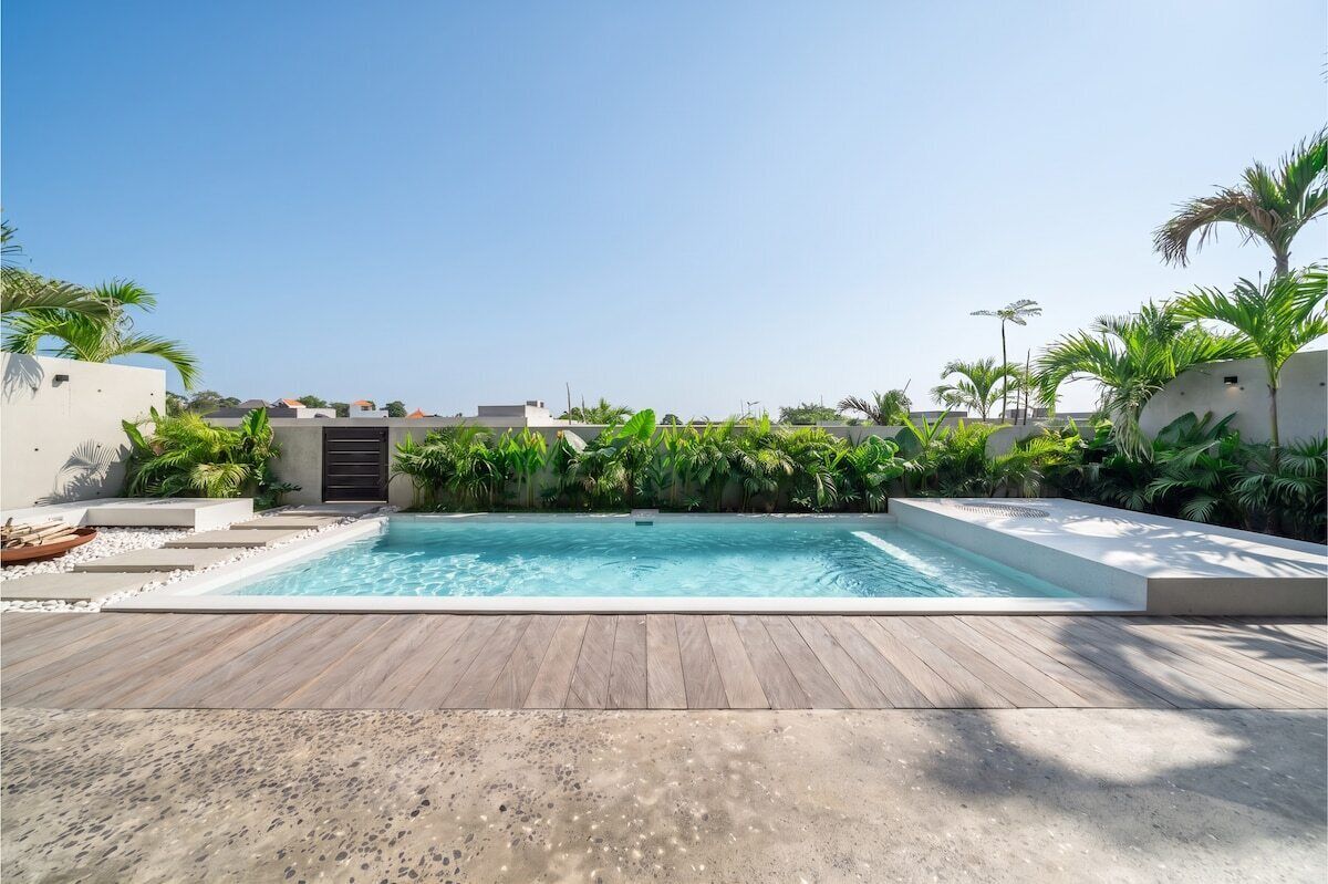 Ein rechteckiger Pool mit Holzterrasse im Vordergrund, umgeben von üppiger Vegetation und Palmen.