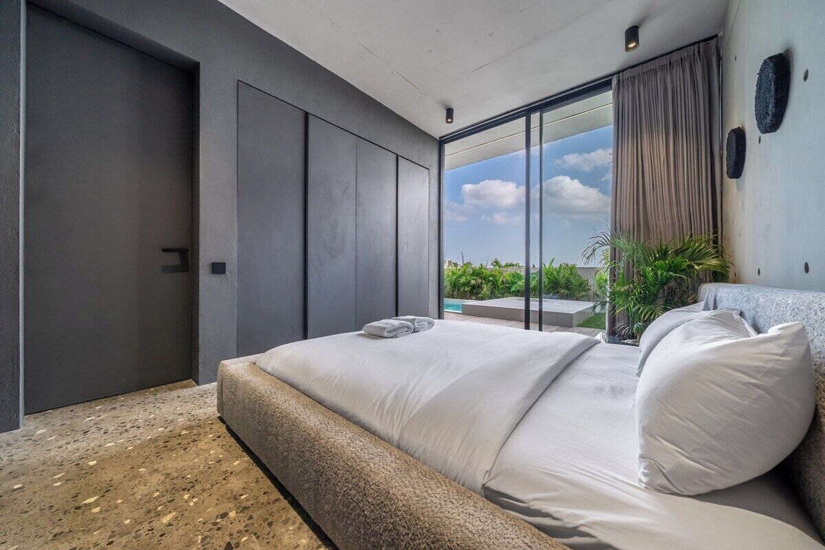 Une chambre moderne avec un grand lit, une porte-fenêtre coulissante donnant sur un balcon et une vue sur la verdure.