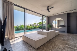 Ein modernes Wohnzimmer mit großem Fenster und Deckenventilator, draußen ist ein Pool zu sehen.