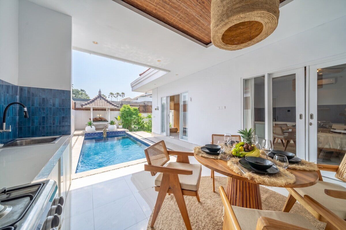 Eine moderne Küche mit integriertem Whirlpool, ein Essbereich mit Tisch für zwei Personen und Blick auf einen Swimmingpool sowie traditionelle Architektur im Hintergrund.