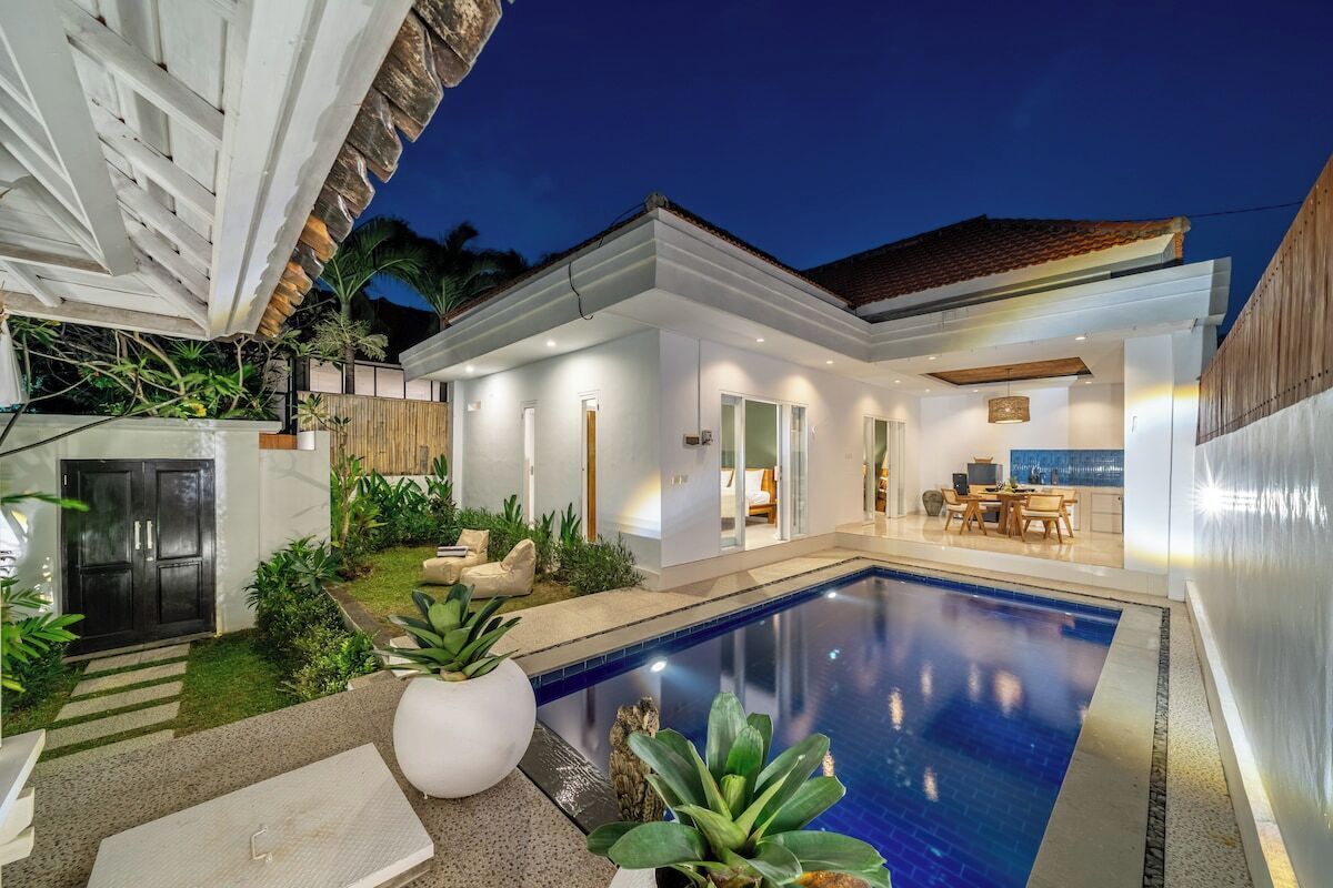 A modern house with a swimming pool, outdoor seating, and a well-lit interior.