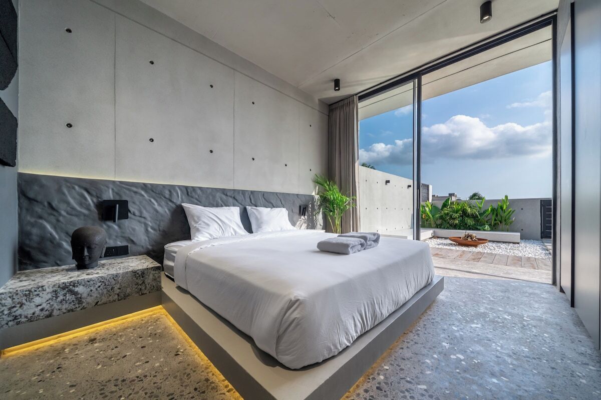 A modern bedroom with a large bed, a marble headboard, and a view of the sky through a sliding glass door.
