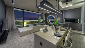 Eine moderne Küche mit Kochinsel, einem Essbereich inklusive Sofa und einem großen Fenster mit Blick auf einen Pool.