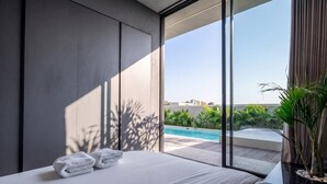 Ein modernes Hotelzimmer mit einem großen Bett, Blick auf einen Swimmingpool und einem Balkon mit Pflanzen.