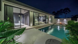 Ein modernes Haus mit Swimmingpool, großen Glasfenstern und einem Feuerkorb.