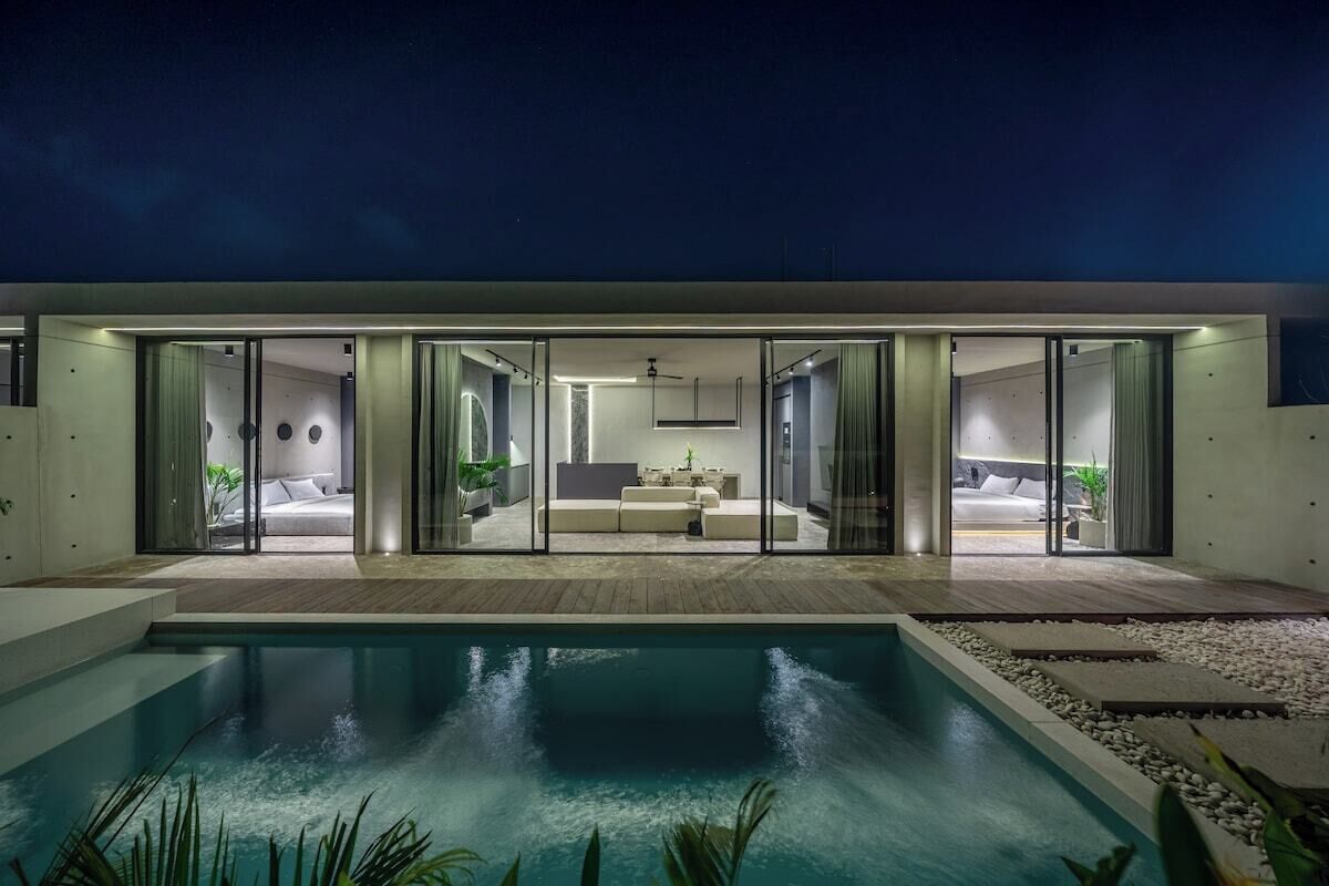 A modern house with a swimming pool, glass doors leading to a bedroom, and a living area with a sofa and coffee table.