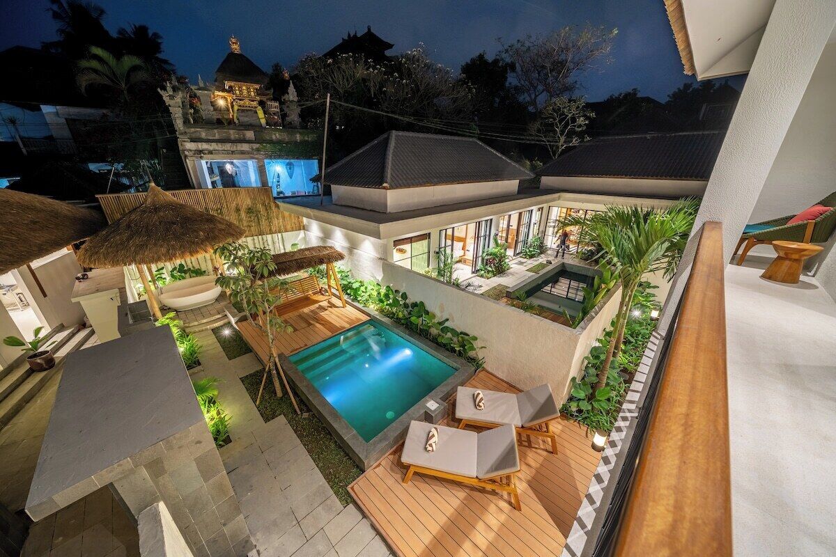 A rooftop pool area with lounge chairs, a hot tub, and a thatched umbrella.