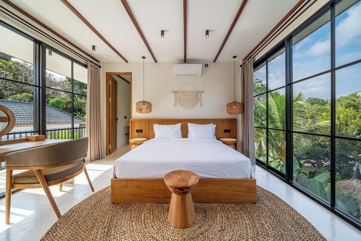 A modern bedroom with a large bed, a desk, and a view of the outdoors.