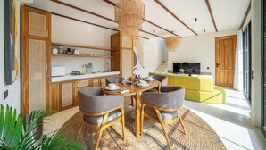 Een moderne woonkamer met een eettafel, stoelen, een gele bank en een keuken met houten kastjes en een wit aanrecht.