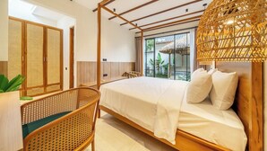 Un dormitorio con una cama, una silla de mimbre, una ventana con vistas y una puerta con un panel tejido.