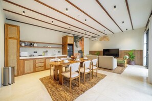 Un salon moderne comprenant un coin repas, un canapé, un téléviseur et une cuisine avec des meubles en bois et un four à micro-ondes.