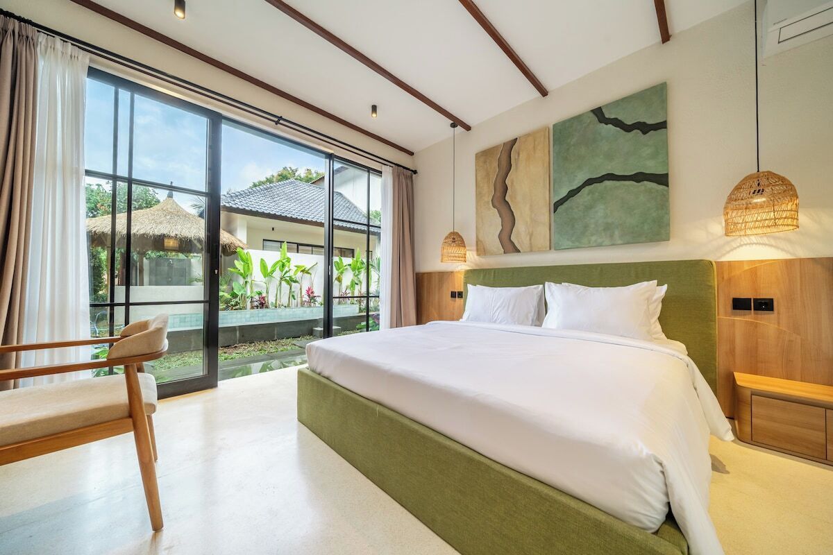 A hotel room with a large bed, a chair, a view of the outdoors, and artwork on the wall.