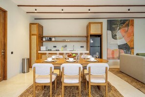 A modern dining area with a wooden table set for four, surrounded by white chairs. - Designer 3BR Villa in Ubud w Pool, Patio & Garden (Gianyar Regency)